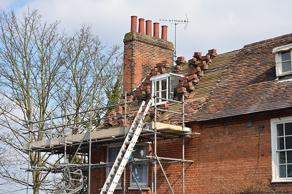 Top of red brick house with a half finished roof repair being done with a scaffolding surrounding